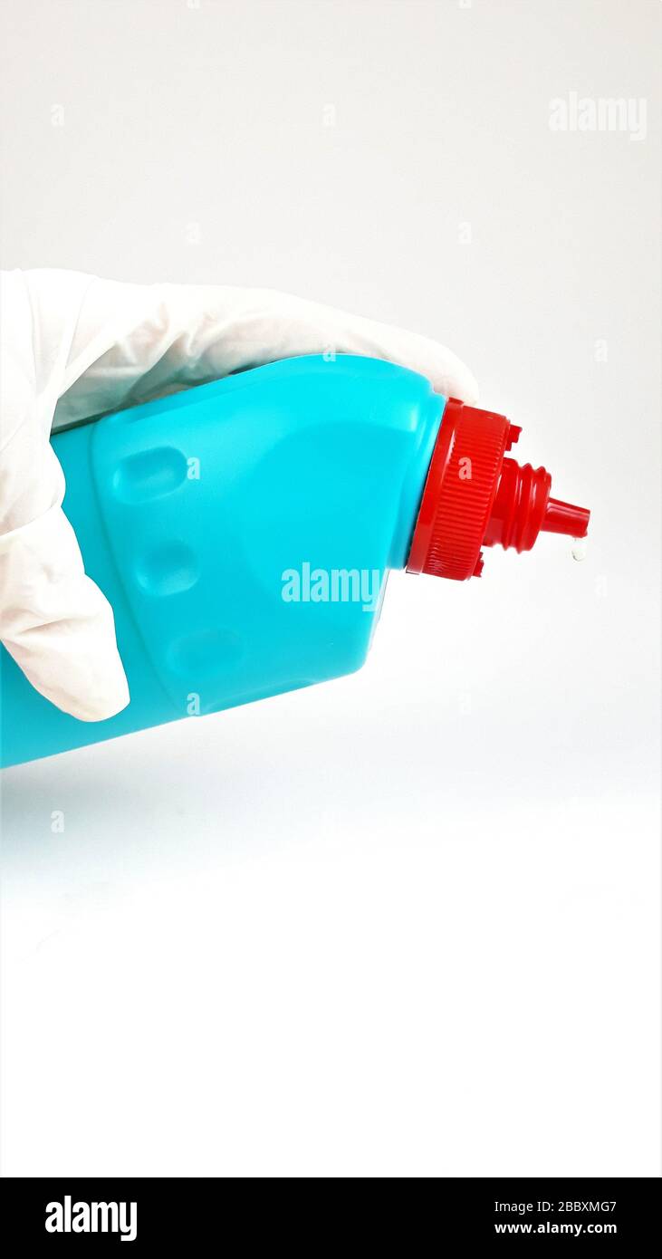 Blue plastic bottle with a red cap in hand in a rubber white glove on a white background.Liquid for cleaning and disinfection of rooms and houses. Stock Photo