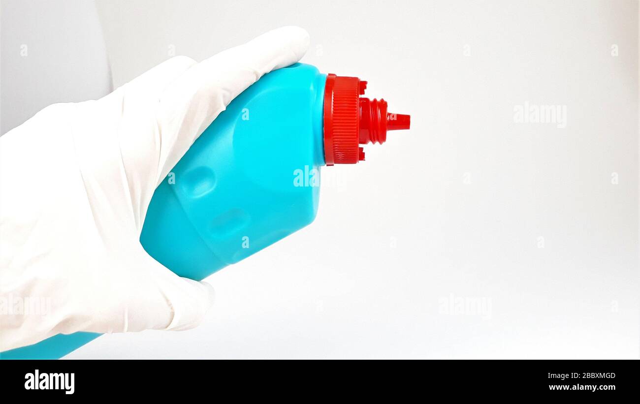 Blue plastic bottle with a red cap in hand in a rubber white glove on a white background.Liquid for cleaning and disinfection of rooms and houses. Stock Photo