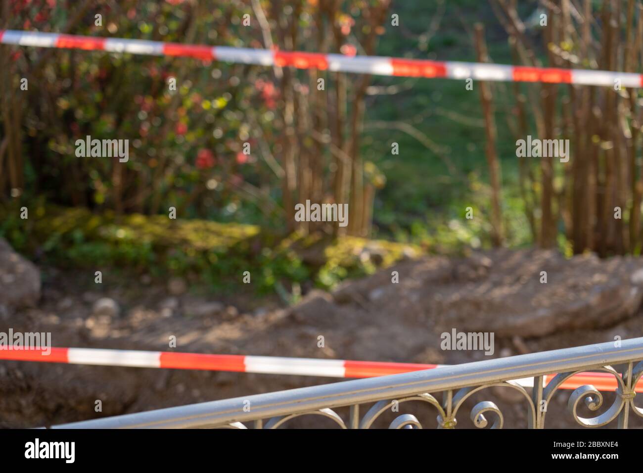 Beautiful ornamented metal fence in foreground. Blurred background with red and white temporary tape barrier in back yard. Space for text. Stock Photo