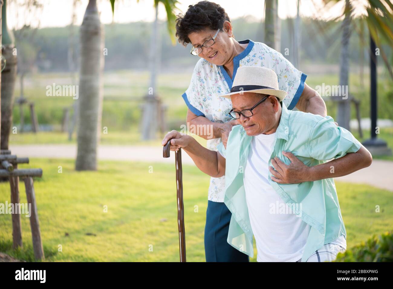 Asian old woman helping an elderly man having having a pain on heart, heart attack in a park. Senior healthcare concept. Stock Photo