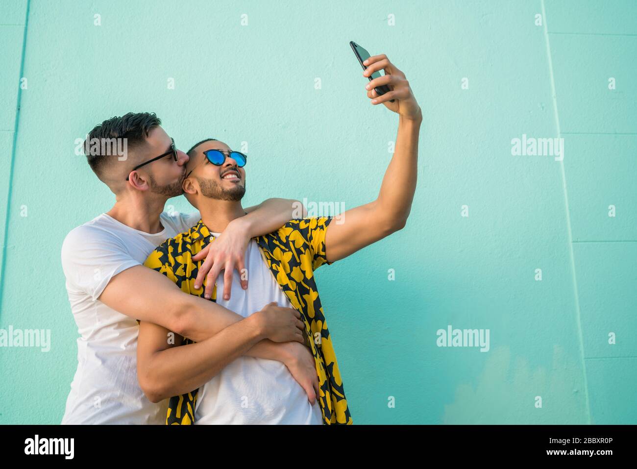 Portrait of happy gay couple spending time together and taking a selfie with mobile phone. Lgbt and love concept. Stock Photo