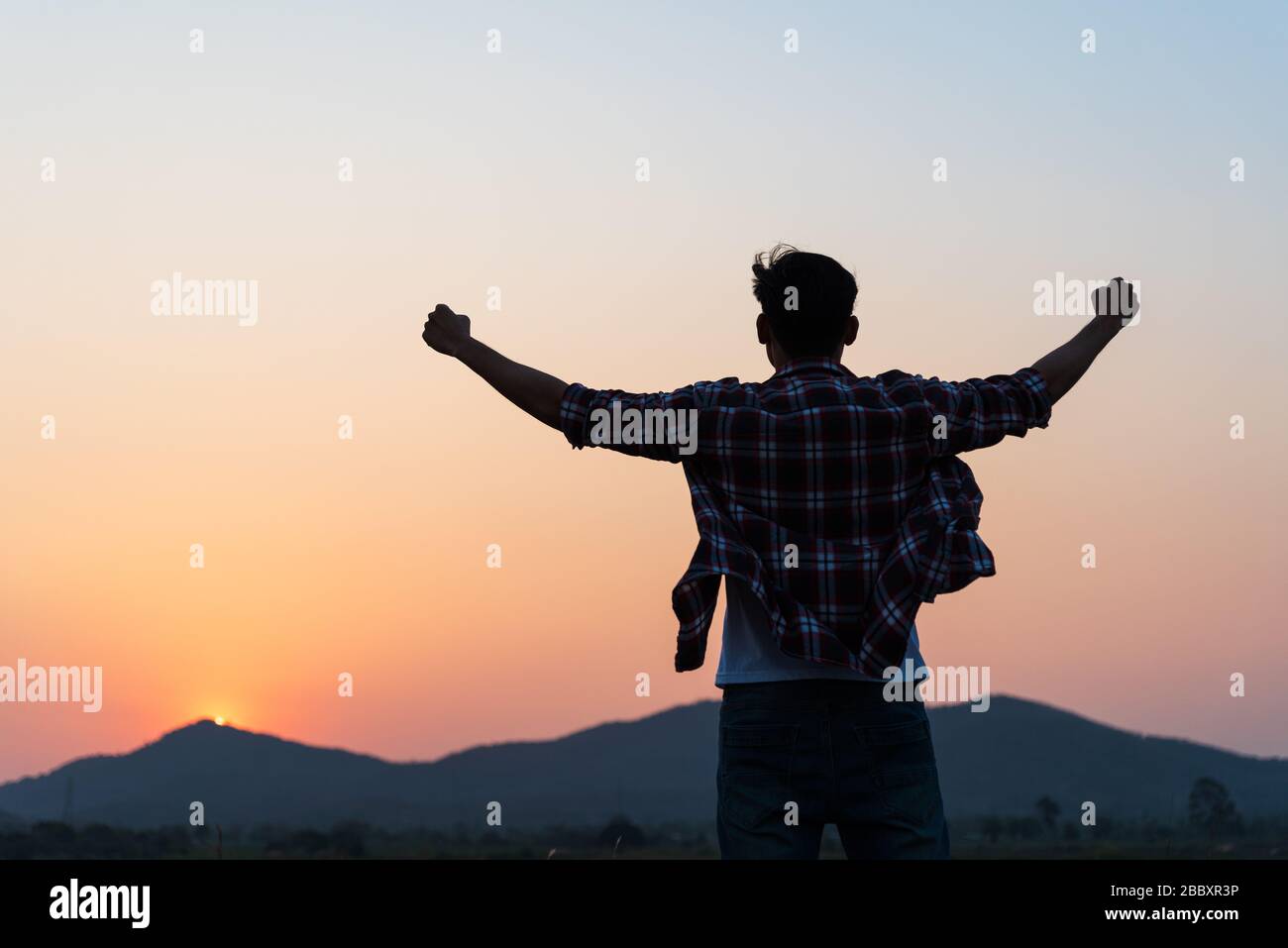 Man with fist in the air during sunset sunrise mountain in background. Stand strong. Feeling motivated, freedom, strength and courage concept. Stock Photo