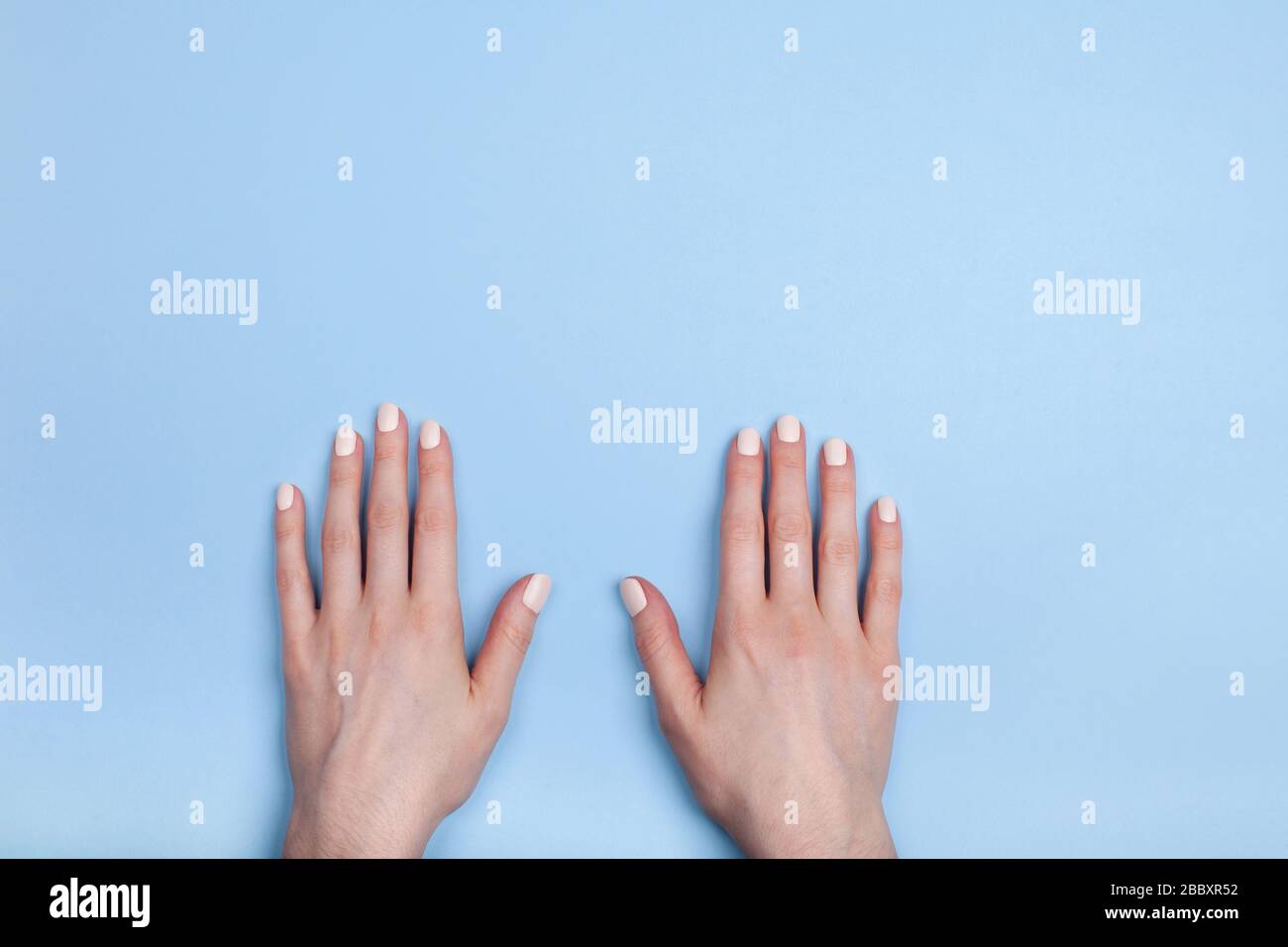Beautiful female hands with a classic matte manicure lie on the table. Place for your text. Stock Photo