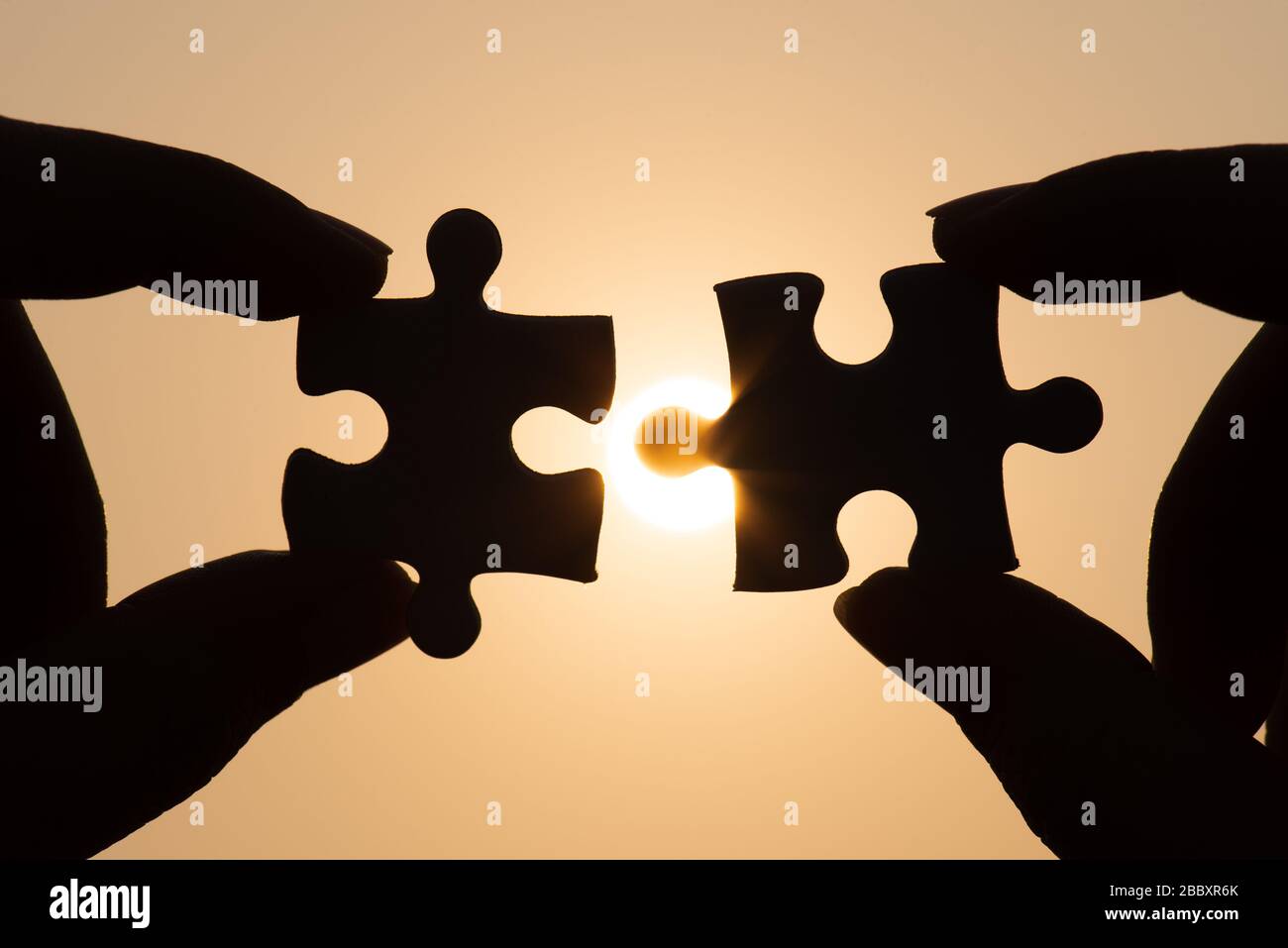 Silhouette of closeup woman's hand connecting a piece of jigsaw puzzle over sunlight effect. symbol of association and connection concept. business st Stock Photo