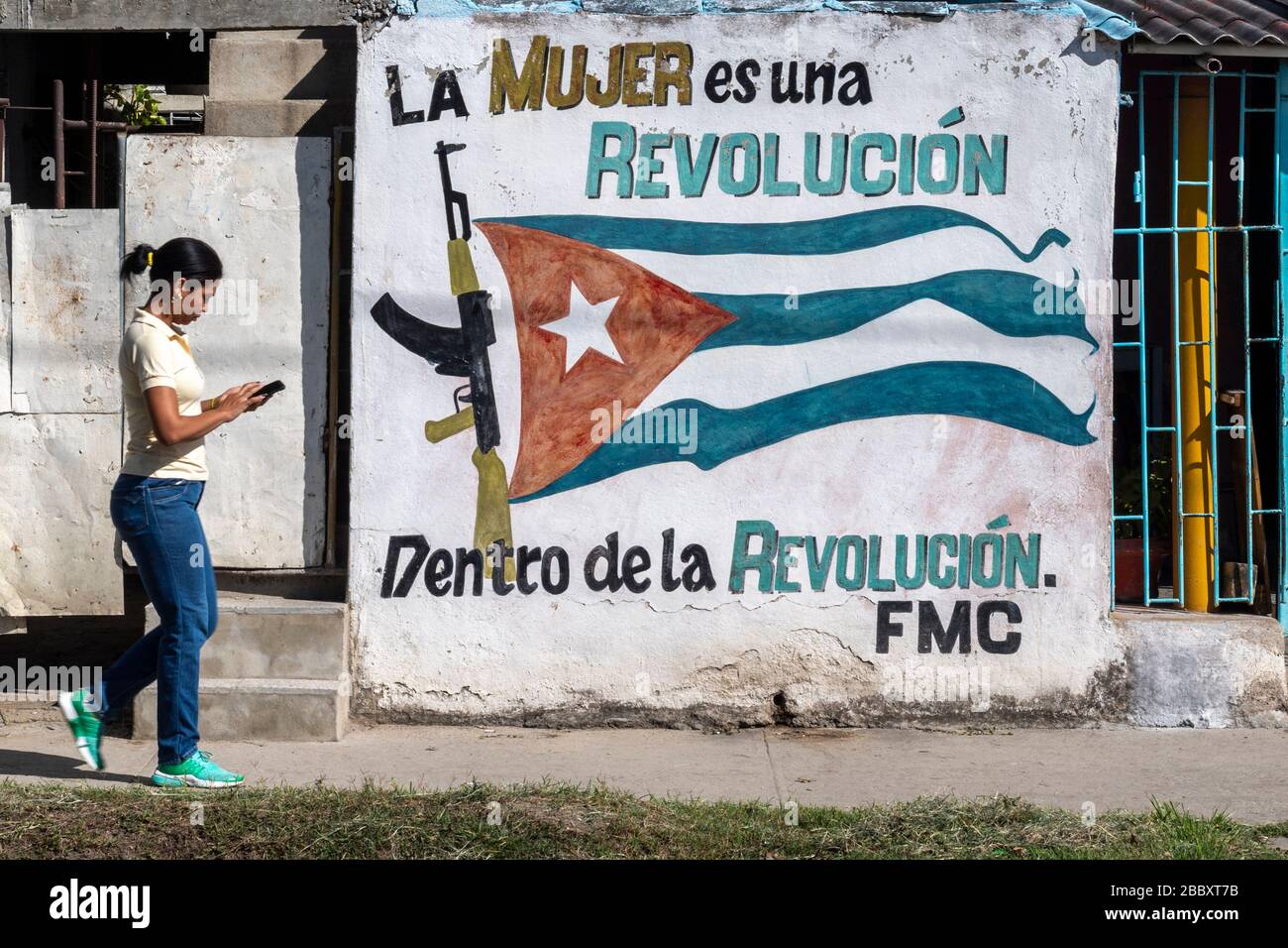 Woman With Mobile Phone Walking Near Propaganda Wall Painting, Cienfuegos, Cuba Stock Photo