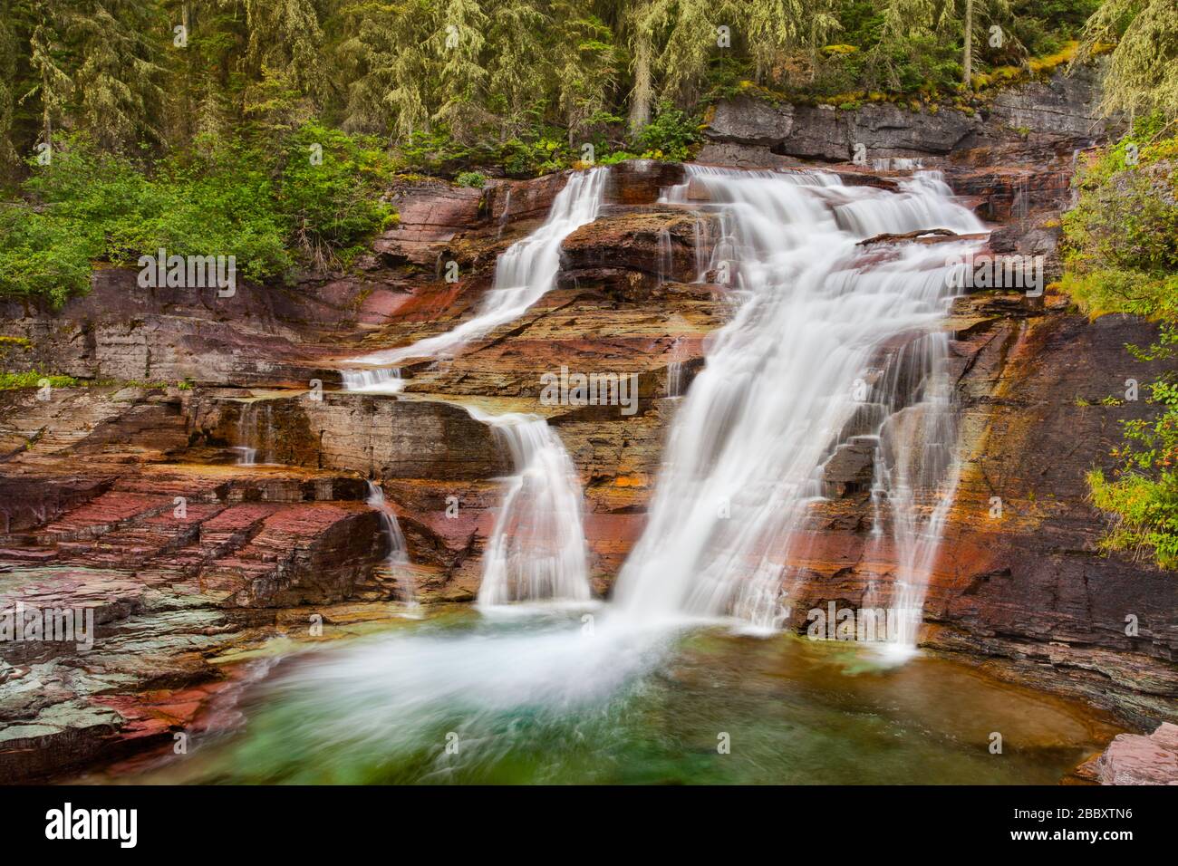 A waterfall cascading over layers of multi-colored rocks in Glacier National Park, Montana, USA Stock Photo