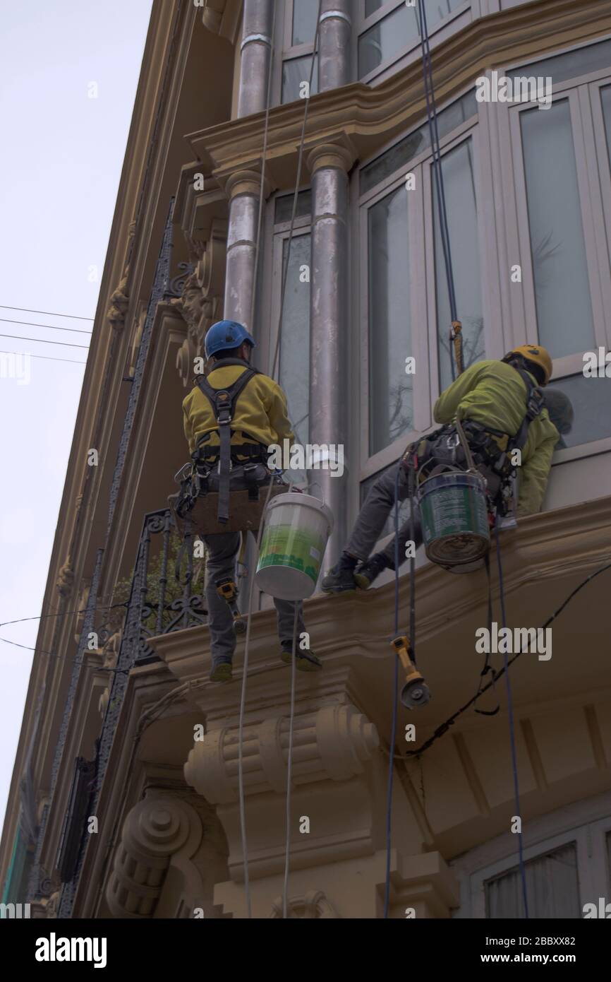 Vertical painters painting an old facade hanging from it in Spain. Stock Photo