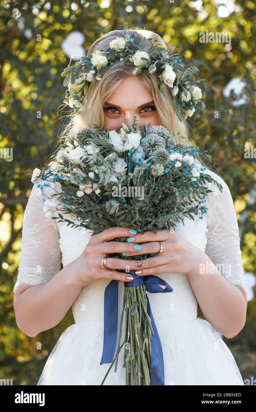 Beautiful blonde young bride portrait with flower bouquet and wreath on ...