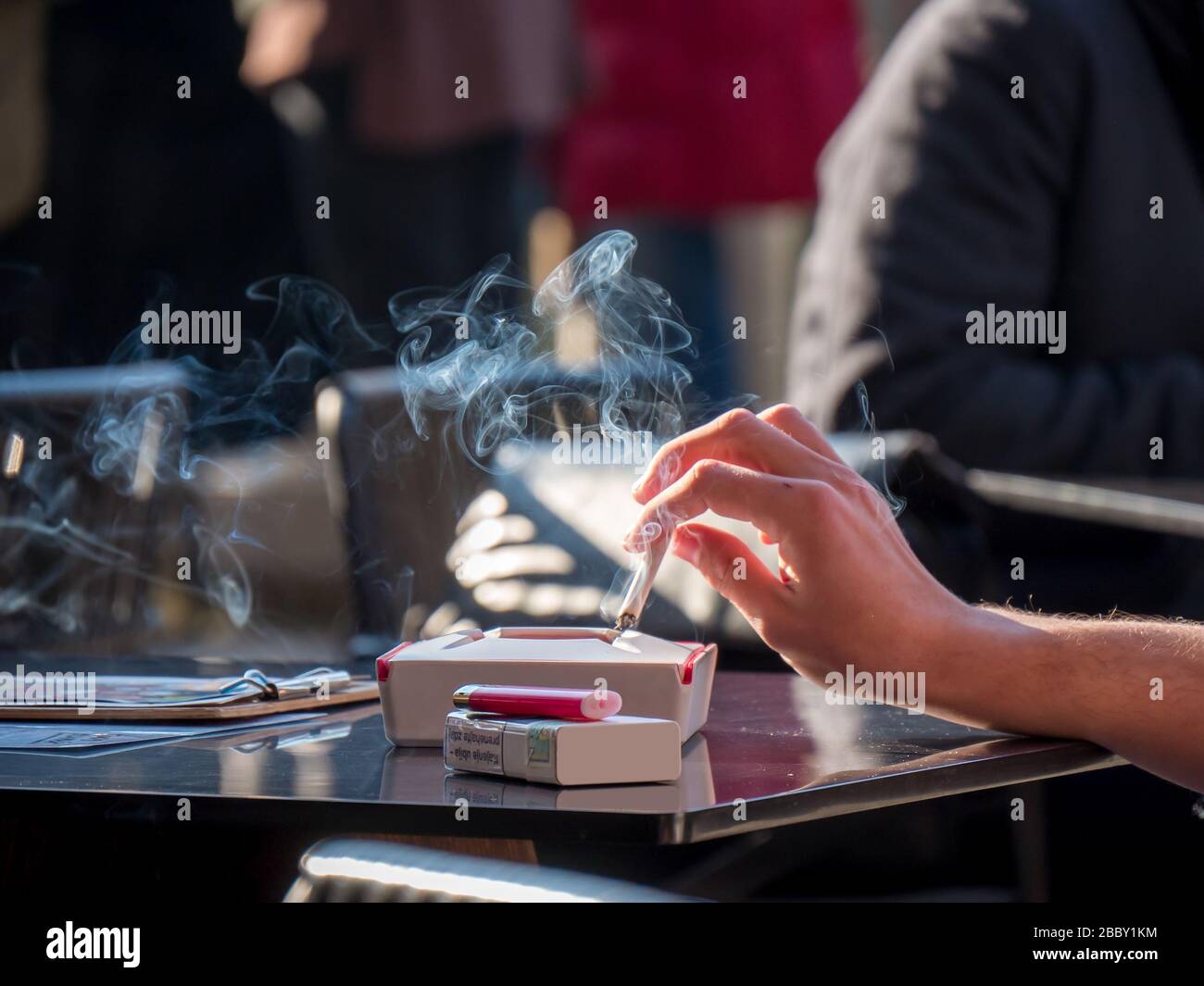 Woman hand holding cigarette with smoke at table. Smoking nicotine addiction unhealthy lifestyle. Stock Photo