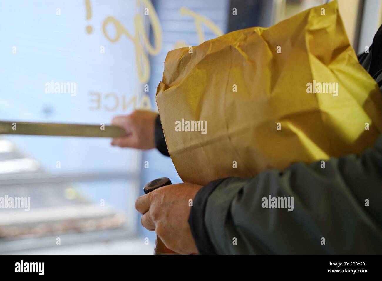 Man pushes the door handle to exit the restaurant after picking up a food order (focus on edge of paper bag) Stock Photo