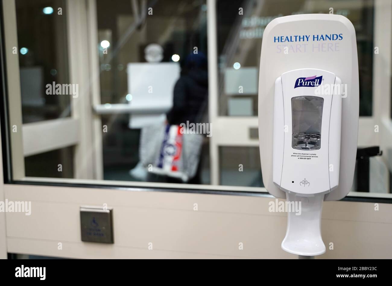 Meriden, CT / USA -  March 16, 2020: A recently used sanitizer dispenser is in the foreground as a healthcare worker in the background exits the hospi Stock Photo