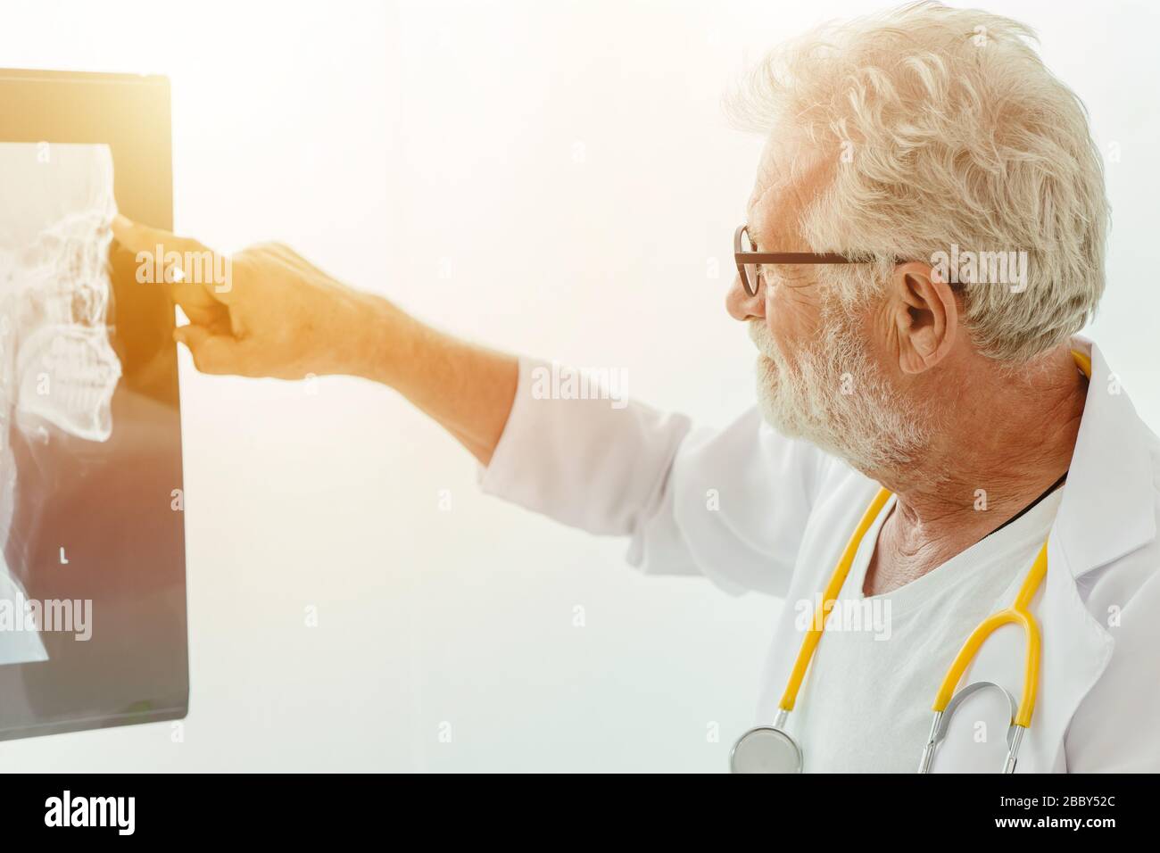 Professional elder doctor looking at x-ray film sheet to find abnormal lump in patient brain. Stock Photo