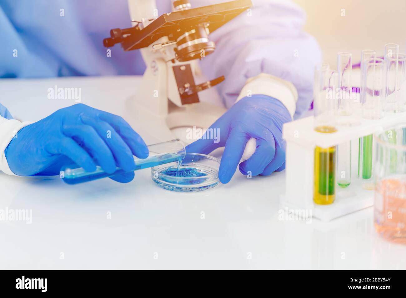 Scientist medical lab technician mixing chemical solution for reaction observing by microscope Stock Photo