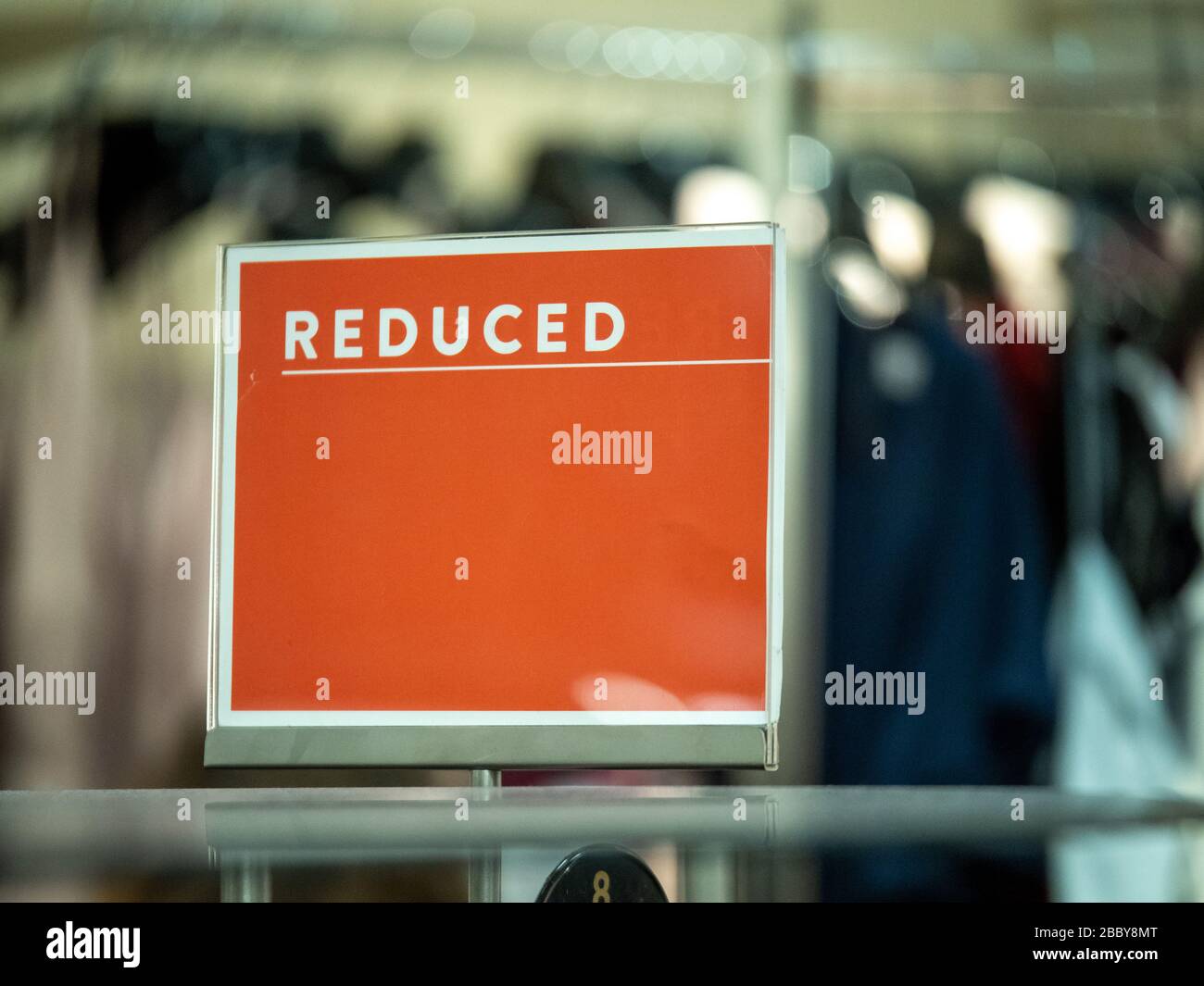 Orange reduced price sale sign on clothing rack in department store Stock Photo