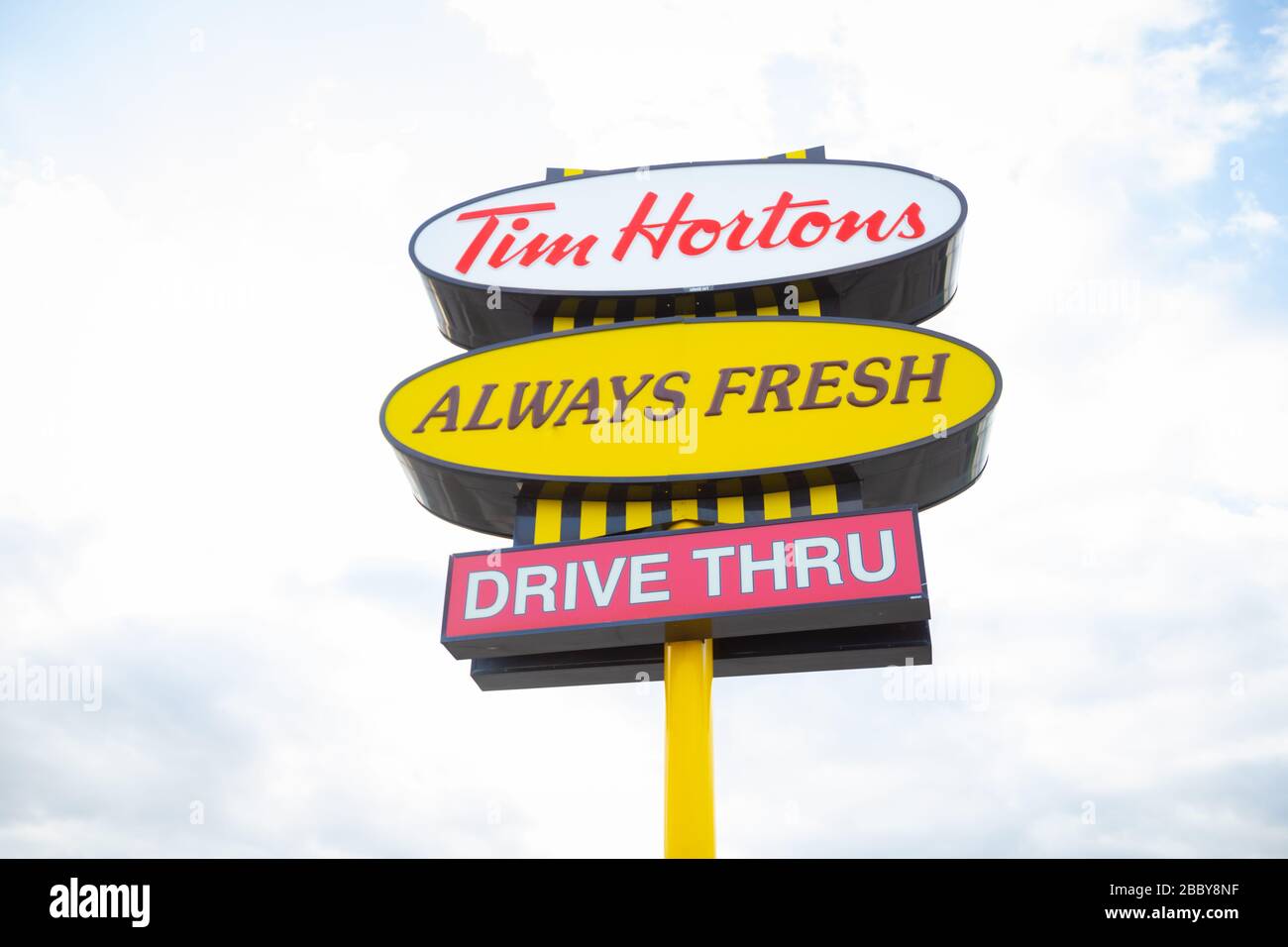 Sign showing Tim Hortons fast food restaurant logo and slogan with sky background Stock Photo