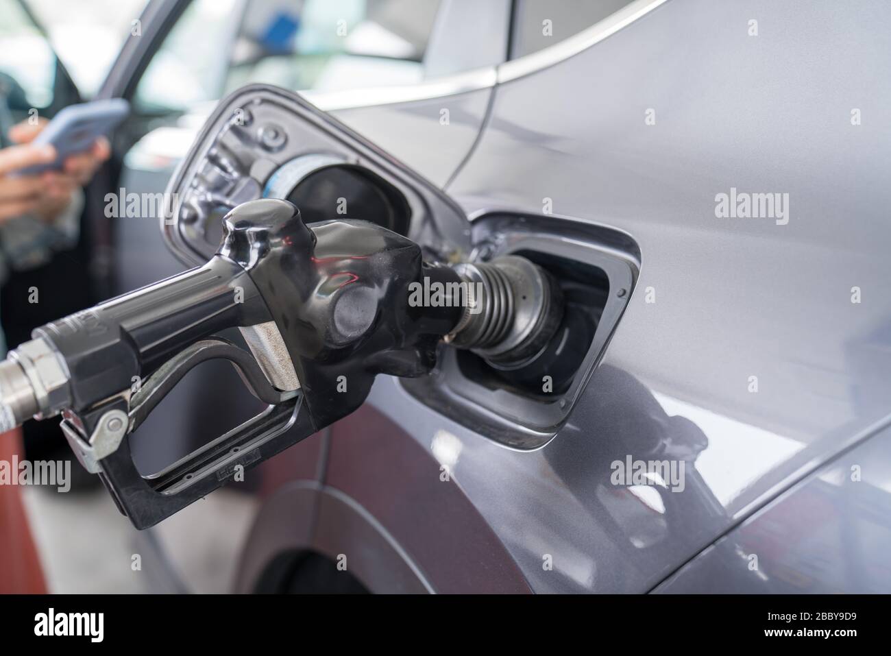 Fuel nozzle refueling a automobile car with woman using phone waiting Stock Photo