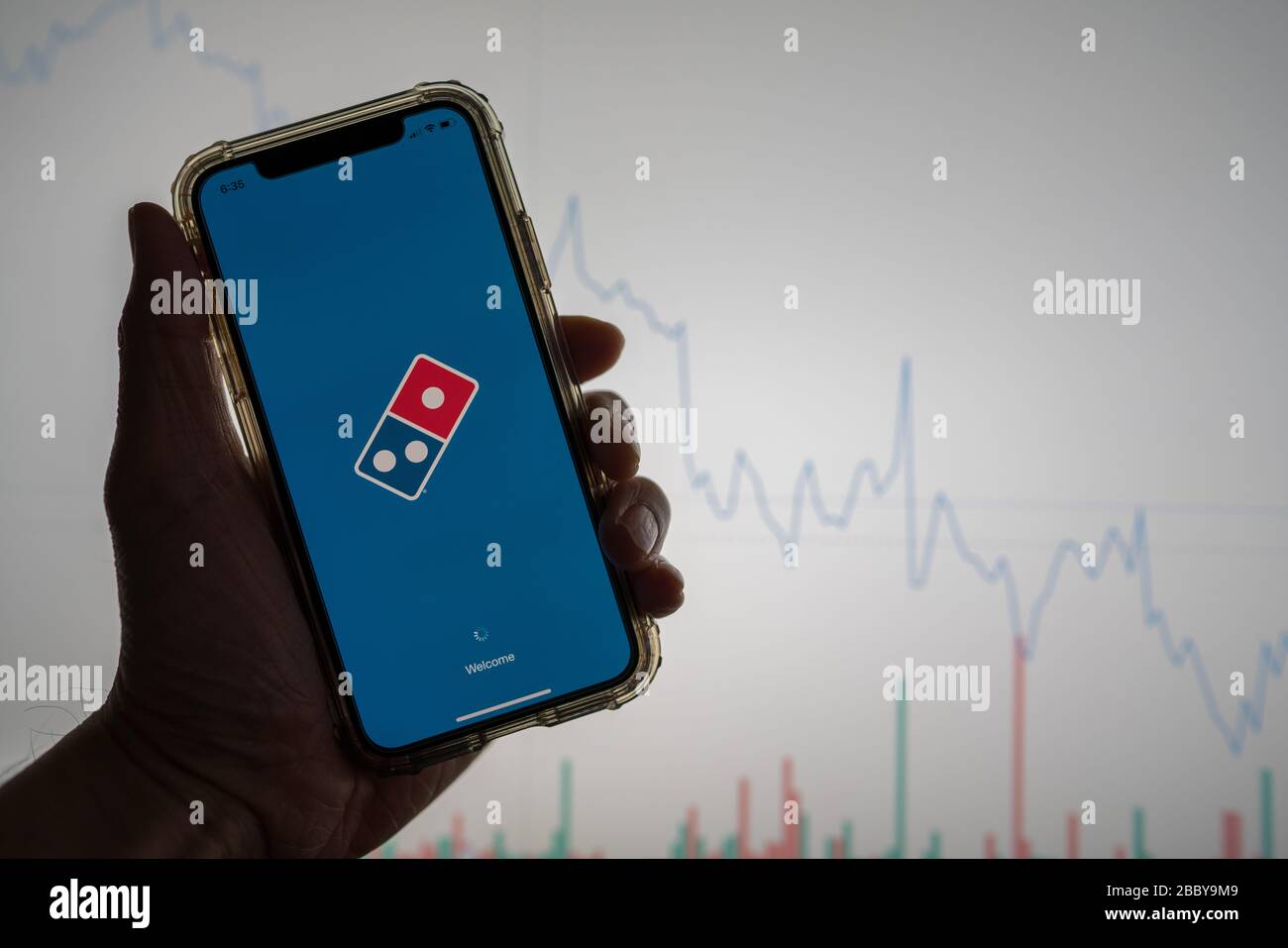 Domino s pizza mobile app held against a white stock trading chart going down in value Stock Photo