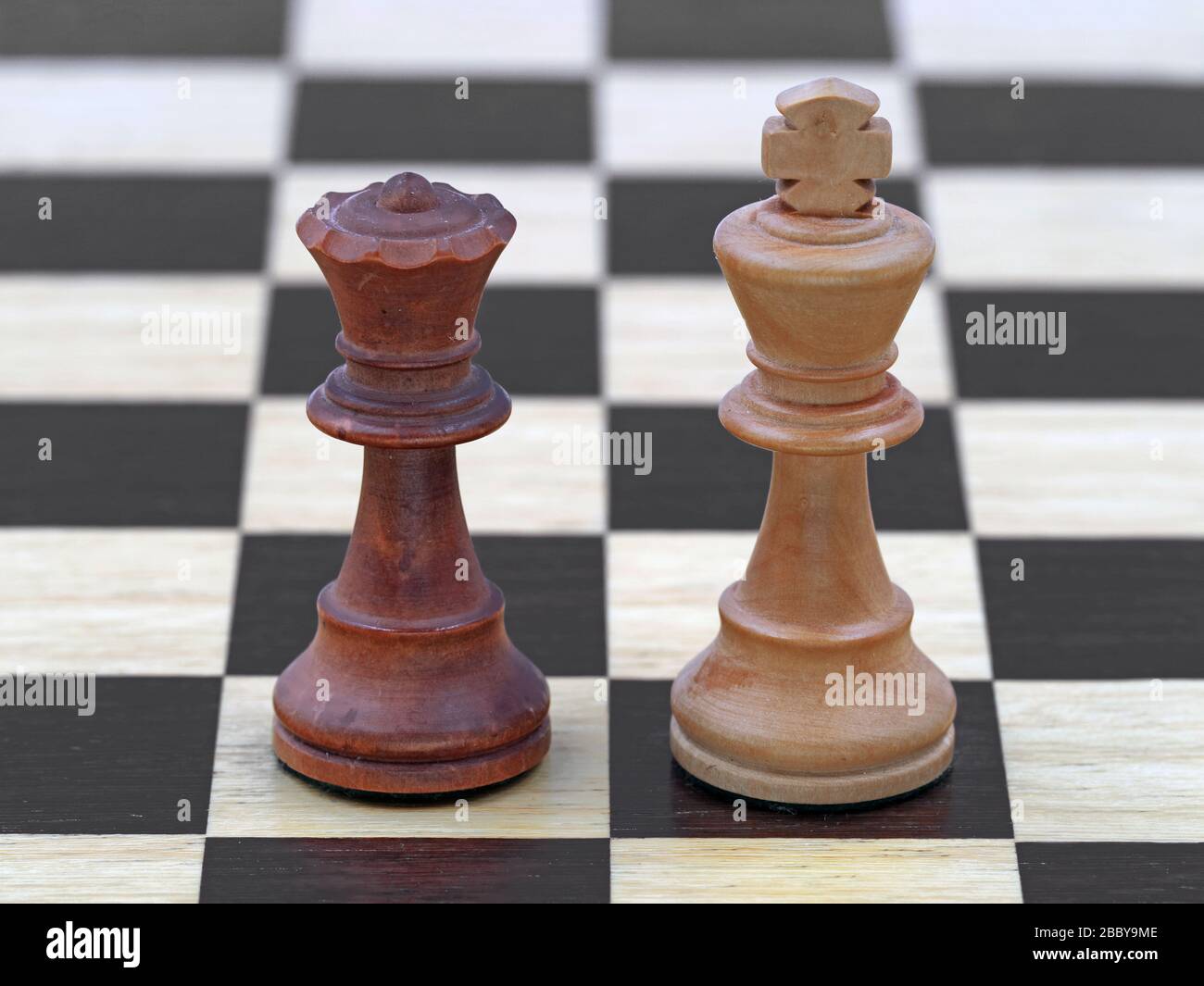 Chess black queen and white king stand on a wooden chessboard Stock Photo