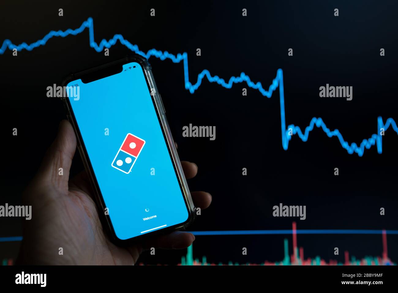 Domino's pizza mobile delivery app held against a dark stock trading chart going down in value Stock Photo