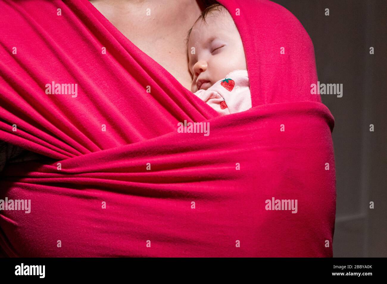 Mother carrying her cute baby daughter in sling. Newborn baby sleeping