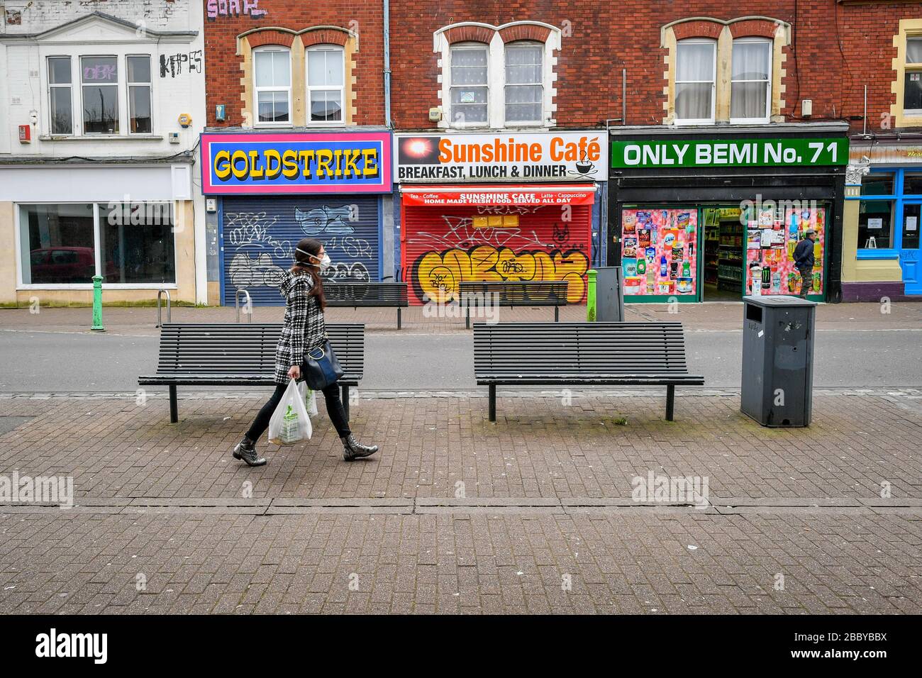 A woman wearing face mask passes shops in Bedminster, Bristol as the UK continues in lockdown to help curb the spread of the coronavirus. Stock Photo