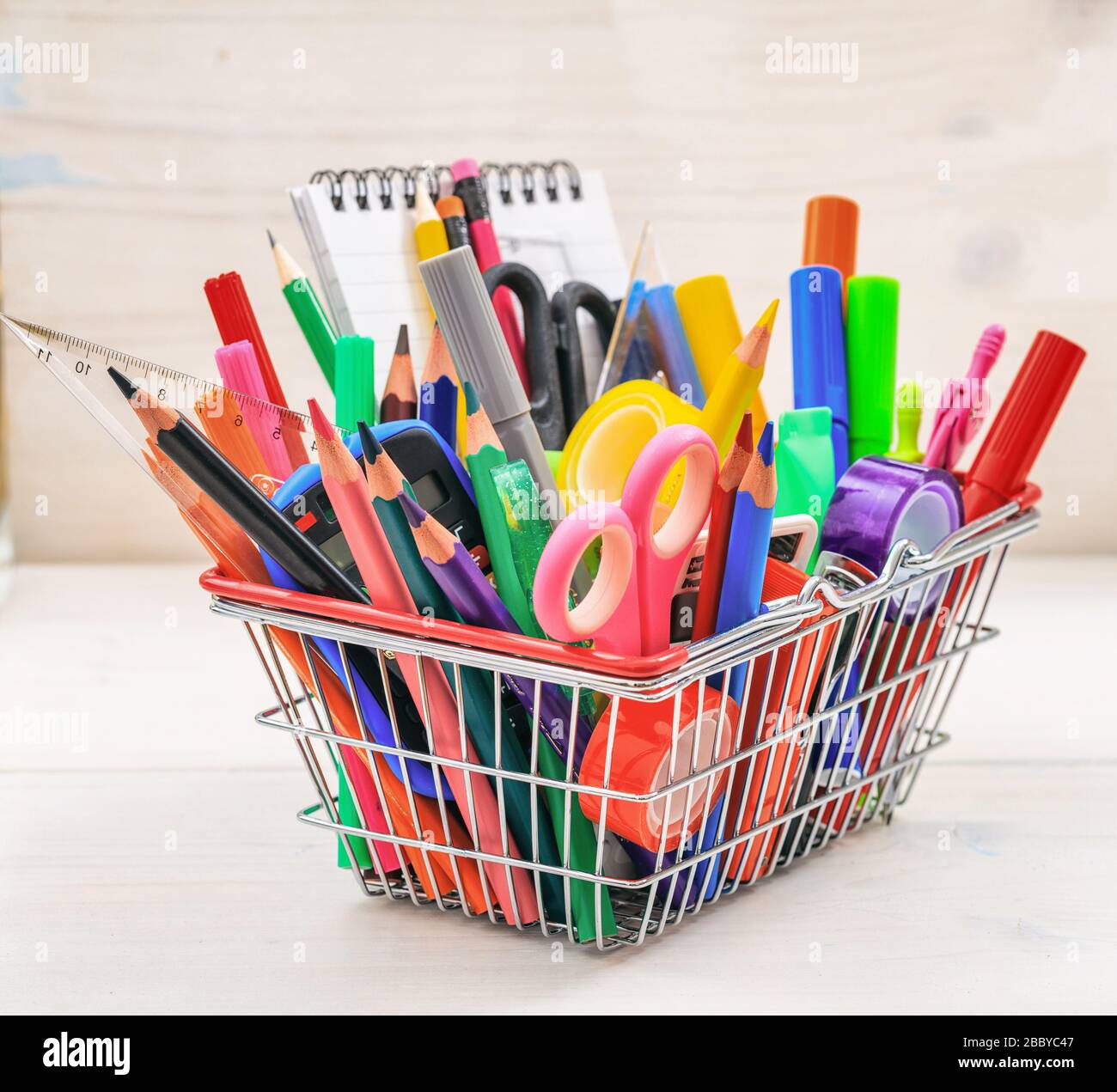 School supplies in a shopping basket, natural wood background. Back to school concept Stock
