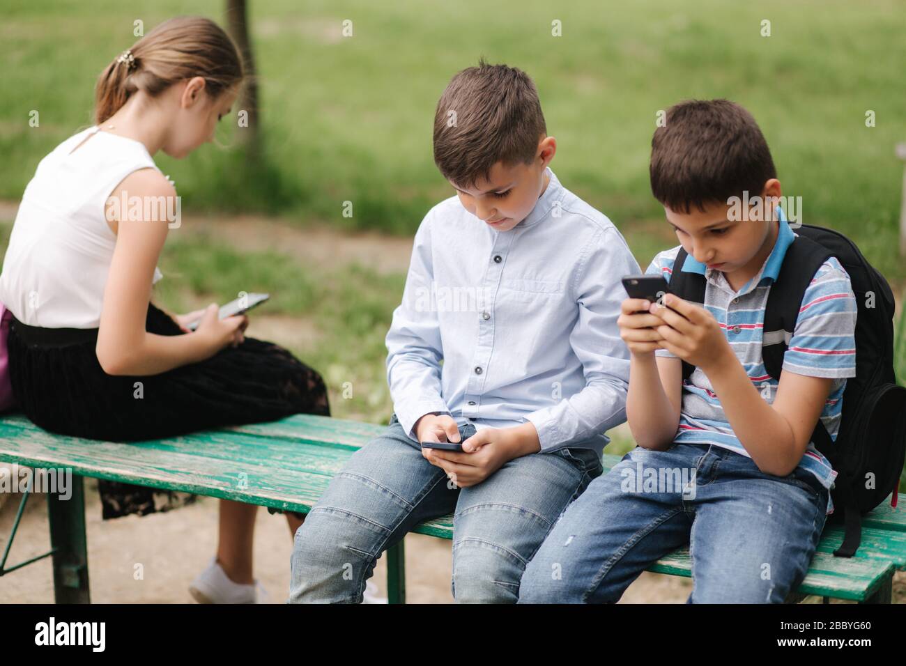 Two boys and girl use their phones during school breack. Cute boys sitting on the bench and play