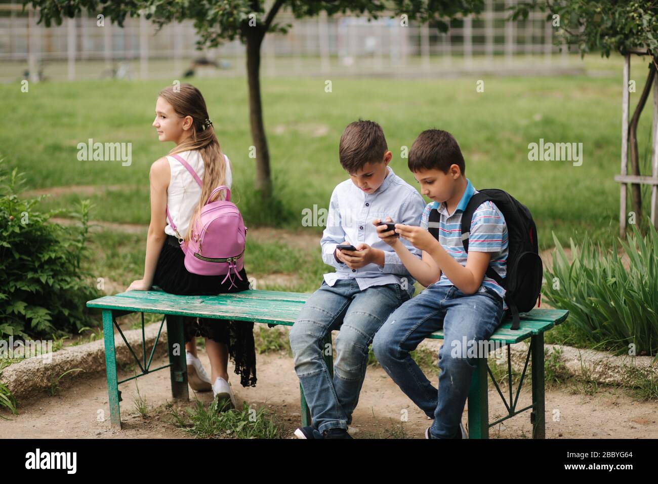 Two boys and girl use their phones during school breack. Cute boys sitting on the bench and play