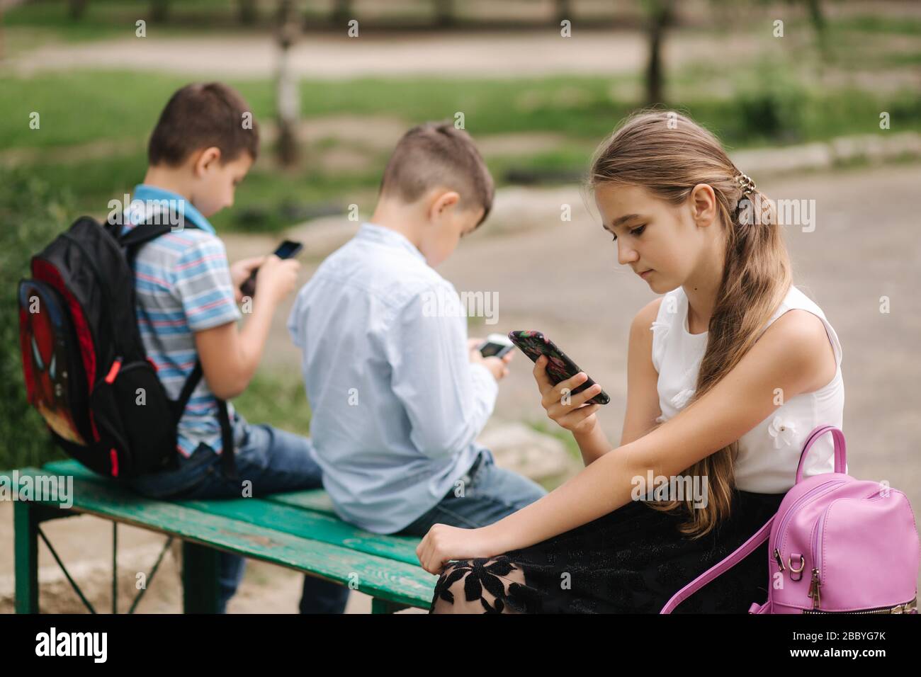 Two boys and girl use their phones during school breack. Cute boys sitting on the bench and play