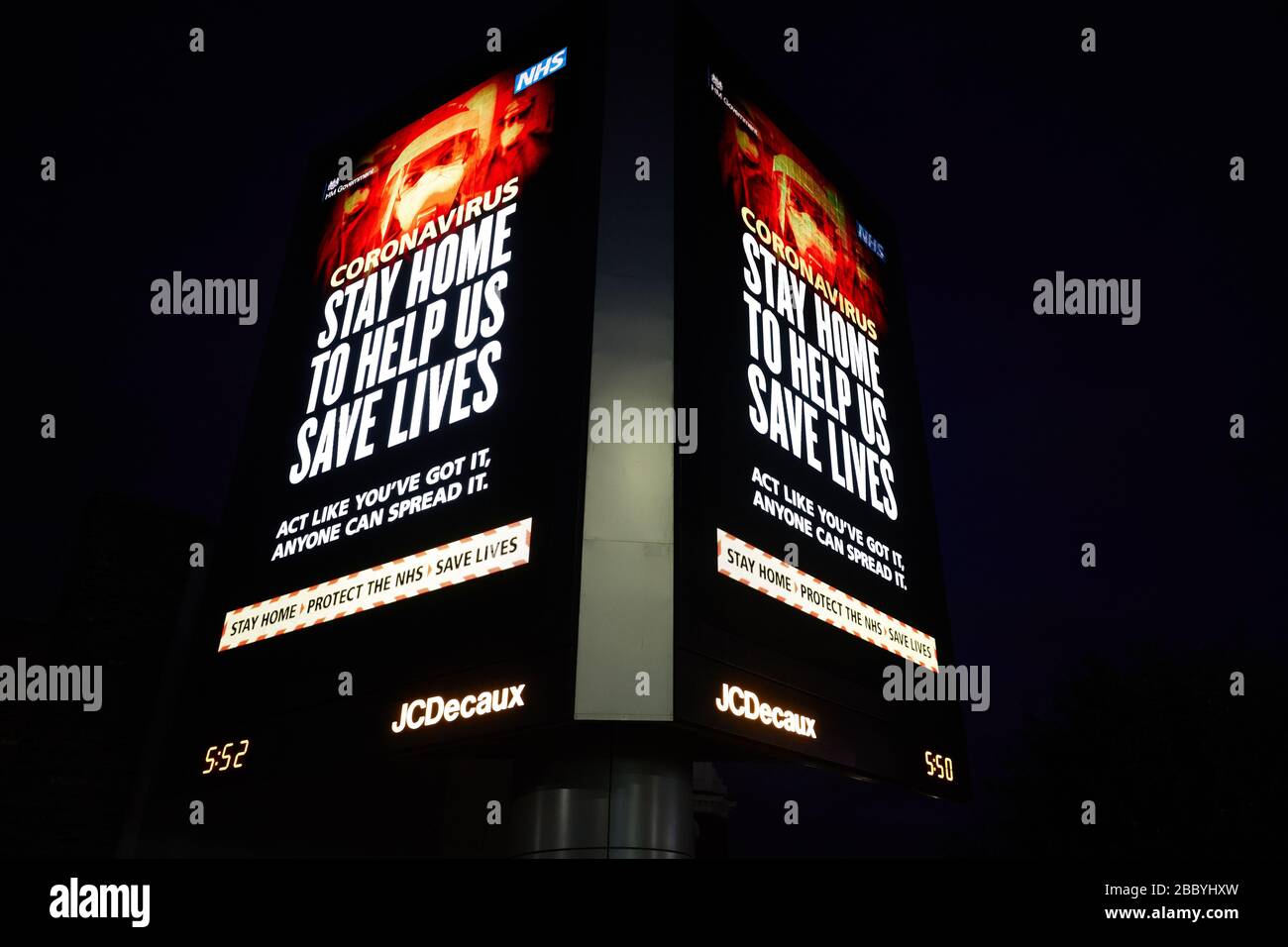 London, U.K. - 02 Apr 2020: A large electronic billboard message from the UK government, warning the public to stay at home during the coronavirus pandemic, lights the night sky. Stock Photo