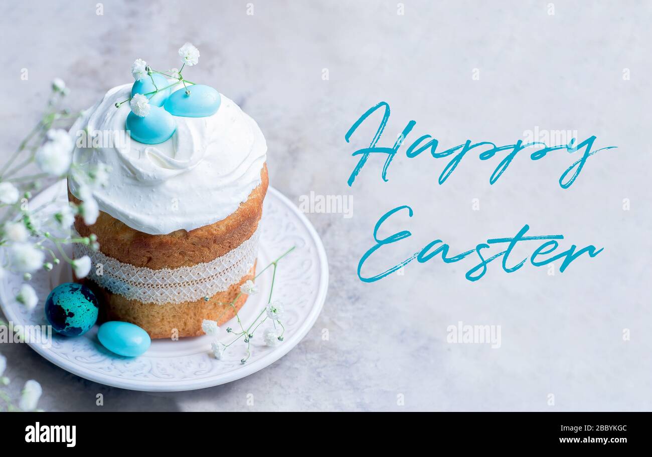 Happy Easter card. Traditional Easter cake kulich decorated meringue and blue candy cane shape eggs on plate on gray stone table background. Stock Photo