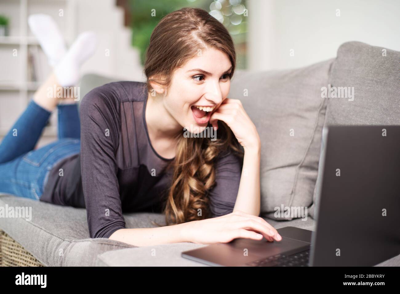 Pretty young woman lying on the couch with a laptop and smiling ...