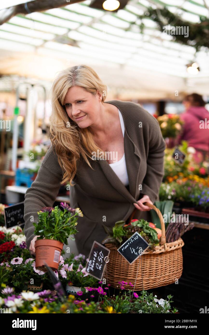 Attractive middle-aged woman happily buys flowers at a market Stock Photo