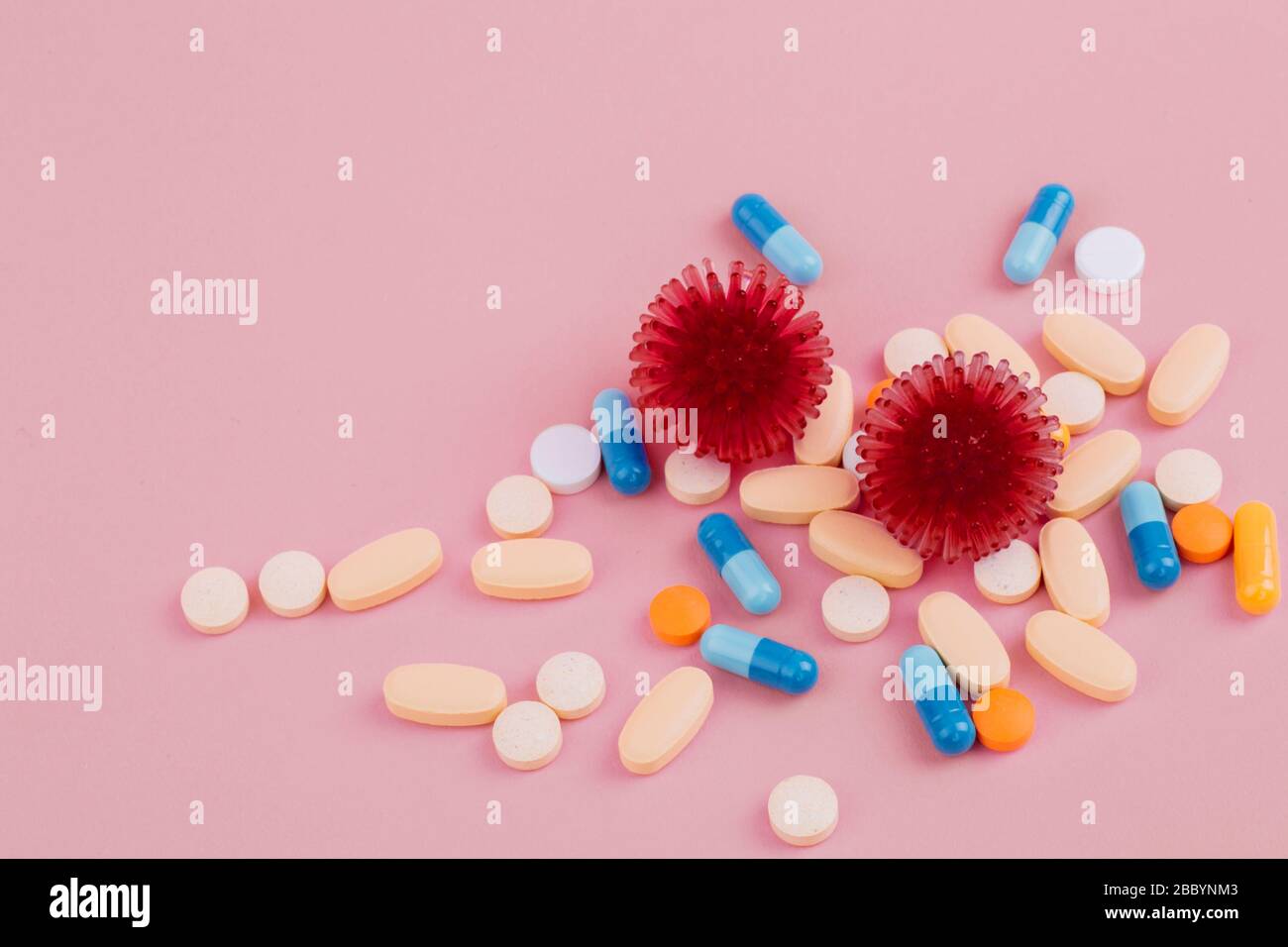 Abstract model of coronavirus infection of the strain Coronavirus. Red virus and a diverse pill on a pink background, the risk of a pandemic. Copy space. Stock Photo