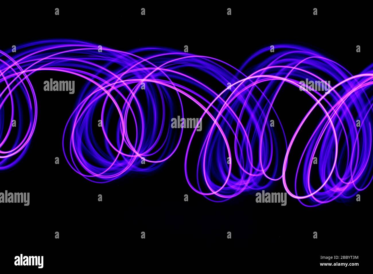 Long exposure photograph of neon purple colour in an abstract swirl, parallel lines pattern against a black background. Light painting photography. Stock Photo