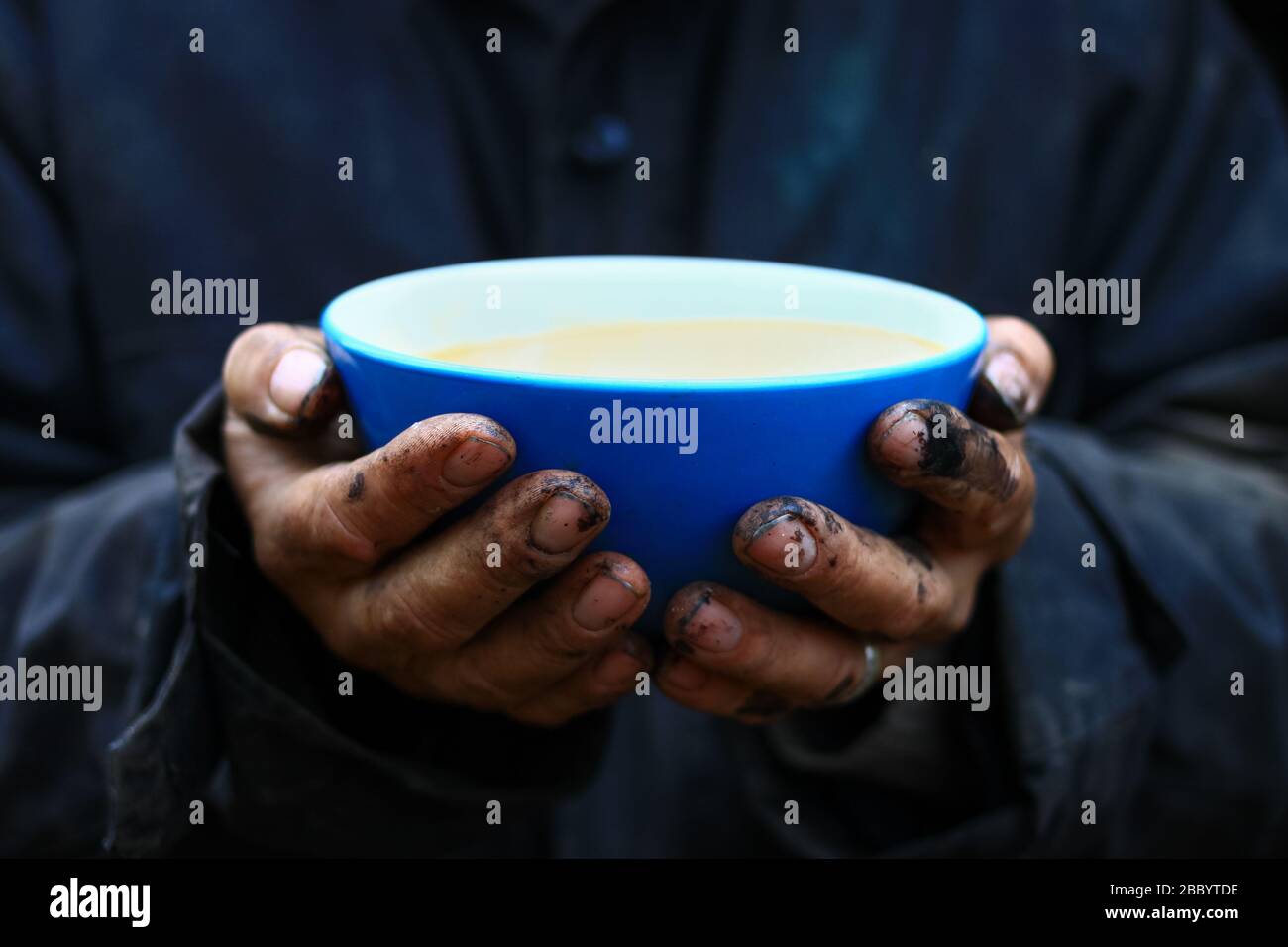 Blue bowl in worker dirty hands with coffee and milk inside (latte) Stock Photo