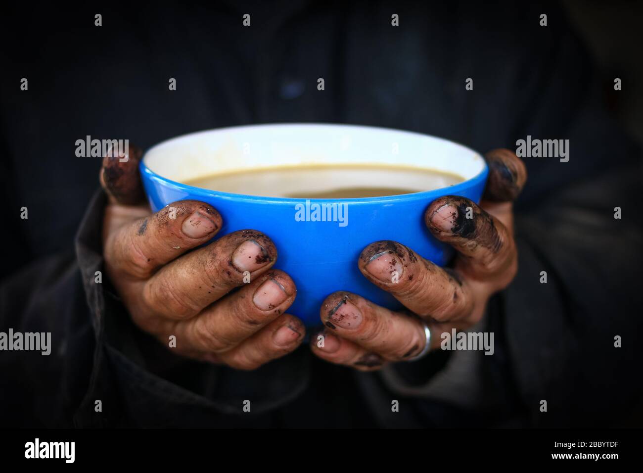 Blue bowl in worker dirty hands with coffee and milk inside (latte) Stock Photo