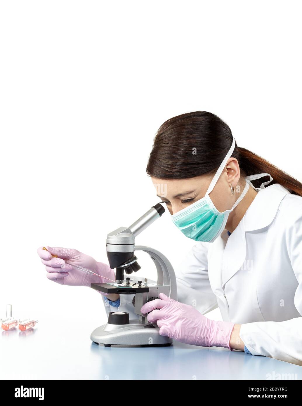 Woman wearing safety gloves and mask doing research with microscope in a laboratory, isolated on white. Stock Photo
