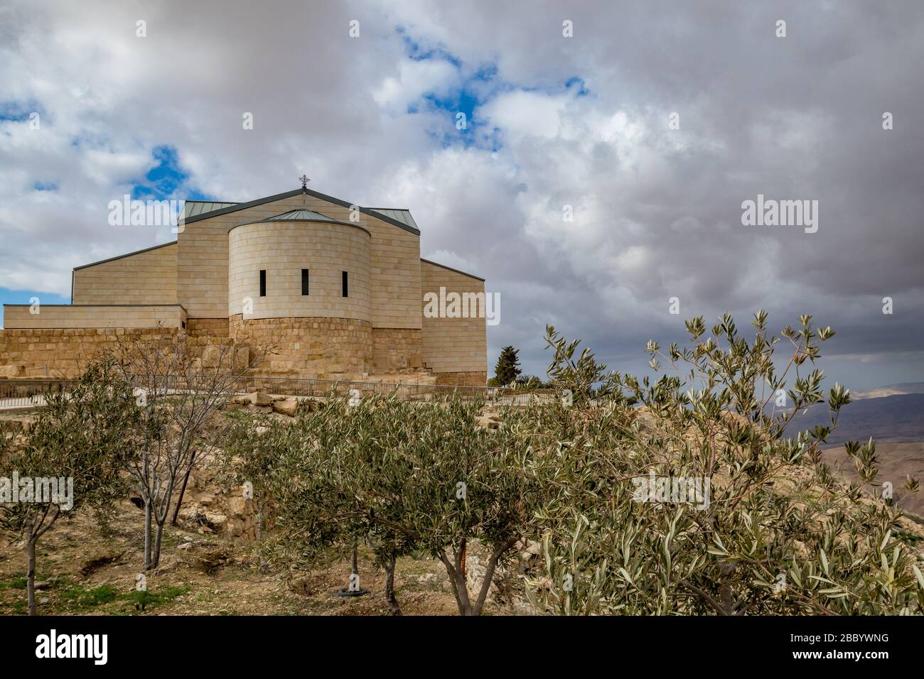 Memorial Basilica of Moses, Mount Nebo, Kingdom of Jordan, cloudy impressive sky winter afternoon. Olive trees in the foreground, performance of Nature and Architecture Stock Photo