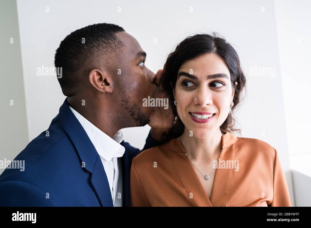 Close-up Of Businessman Whispering Into Female Partner's Ear Stock Photo