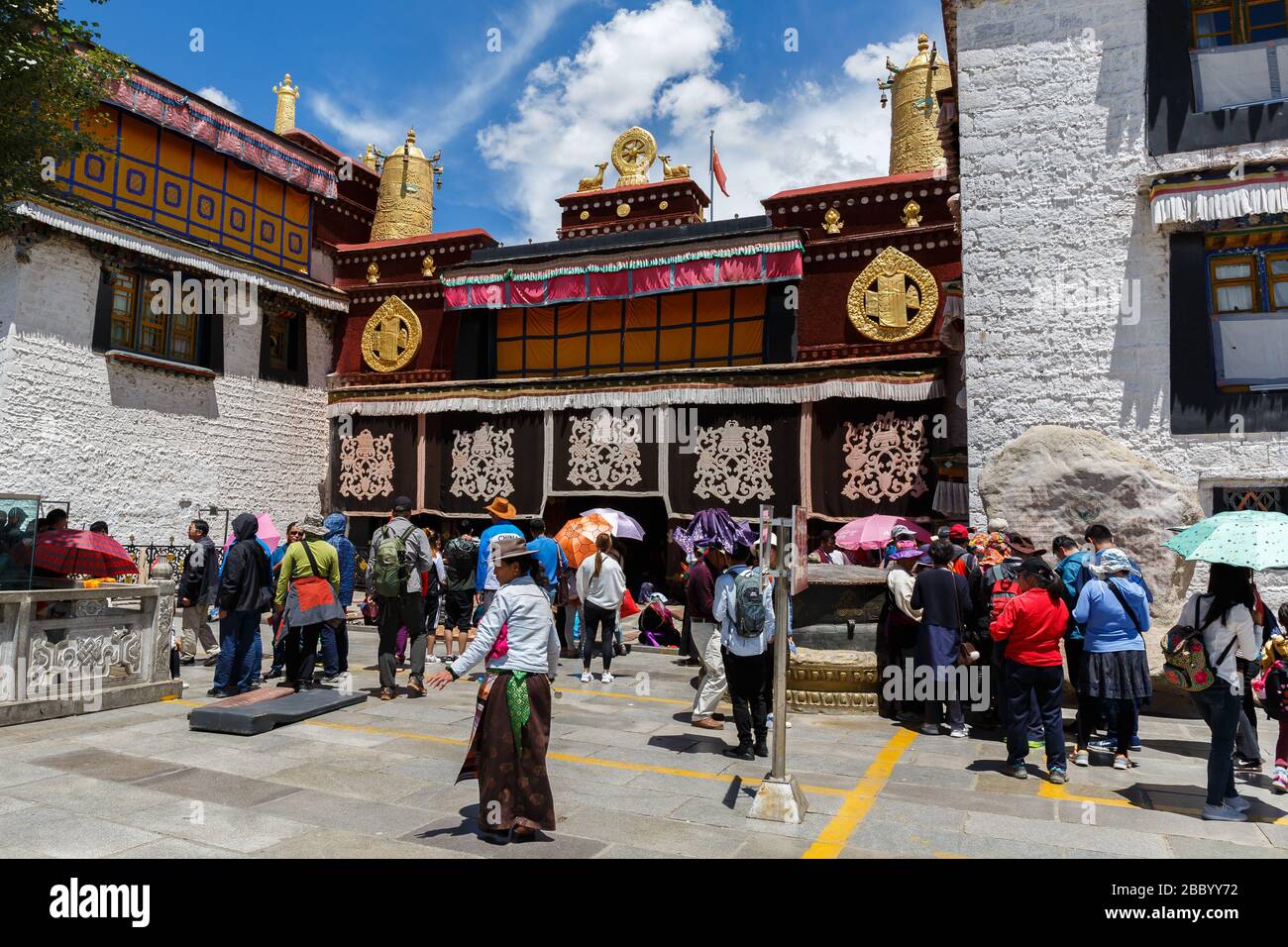 Visitors - both pilgrims & tourists in front of Jokhang temple. One of Tibets tourist magnets. Detail: Chinese flag next to the golden Dharma wheel. Stock Photo