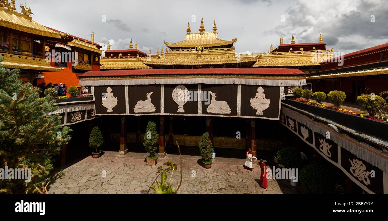 Panorama view of rooftop and yard with monks of Jokhang Temple (Unesco World Heritage). Most important rooftop features: Dharma wheel and deers. Stock Photo