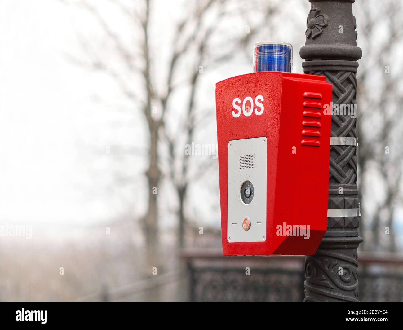 Help or police call button. SOS. A stand with a button is fixed on the street, on a lamppost. Red housing with blue warning light on top. Stock Photo