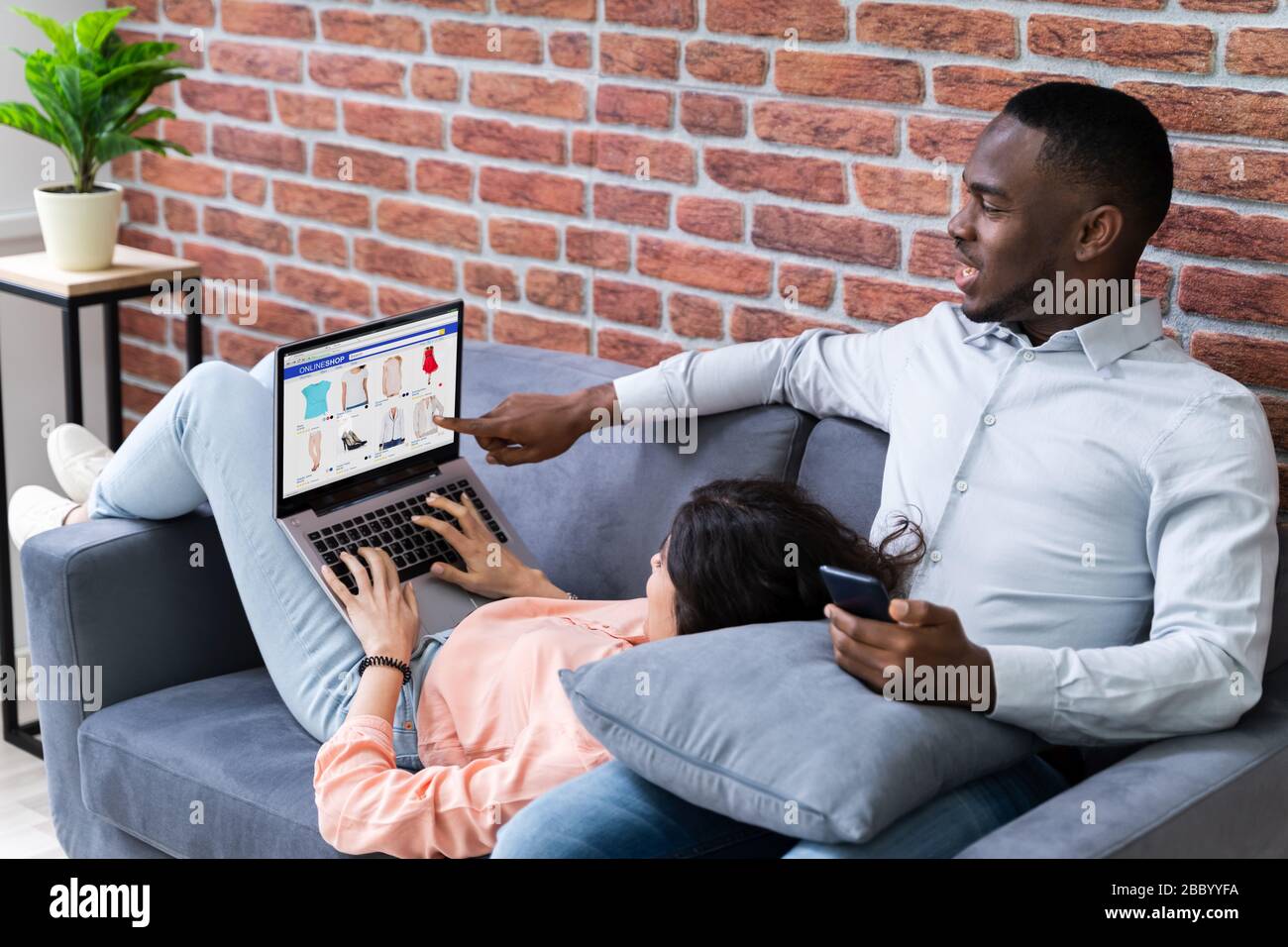 Couple Using Laptops While Relaxing On Sofa At Home Stock Photo