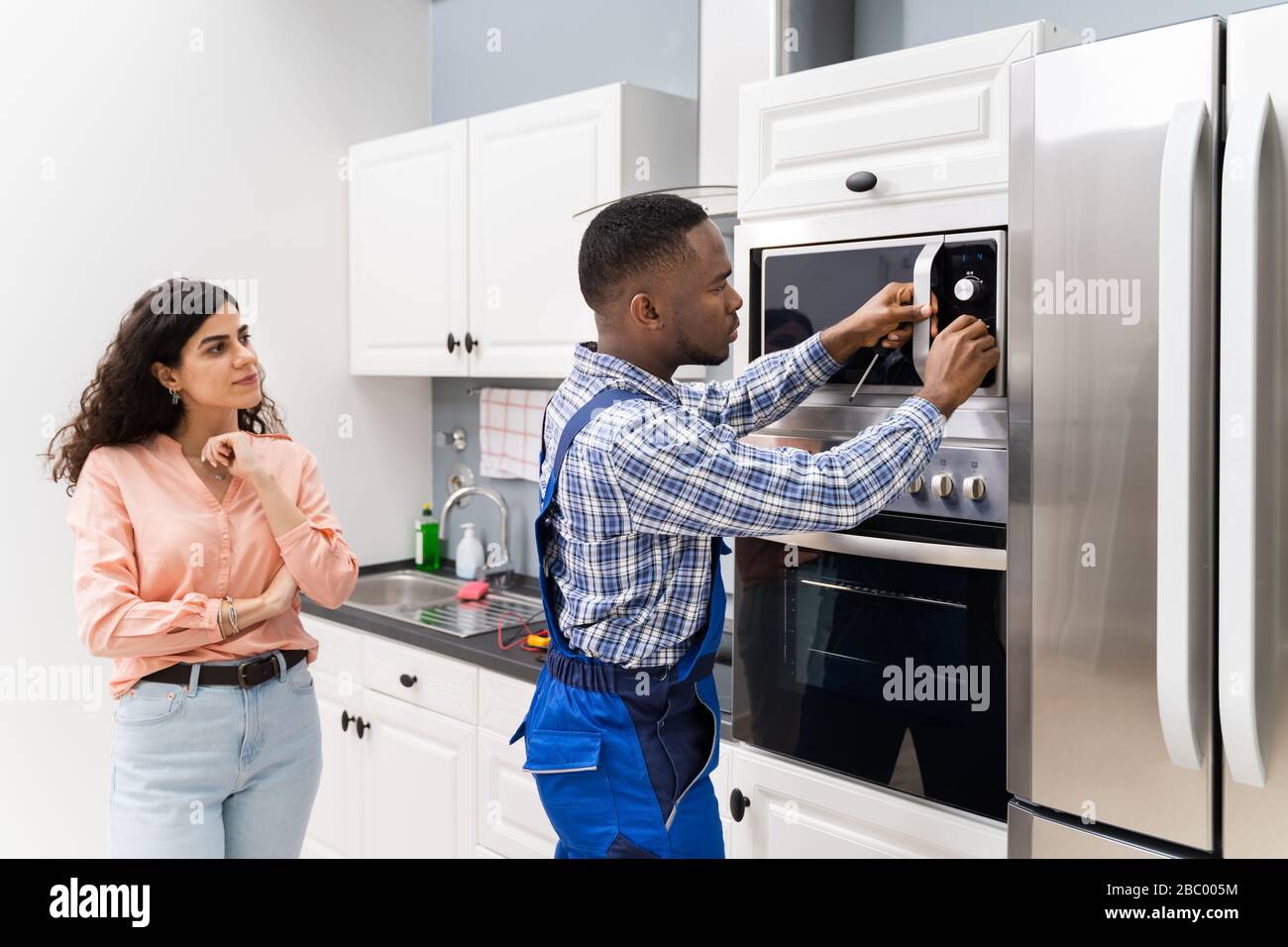 Happy Young Woman Standing Near Technician Adjusting Temperature Of Oven Stock Photo