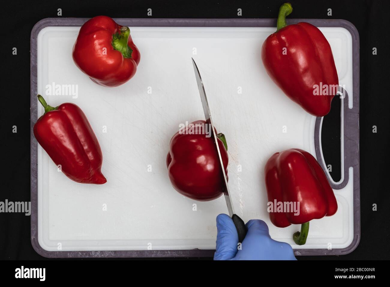 A man in blue hygiene gloves cuts red sweet peppers at home, caution