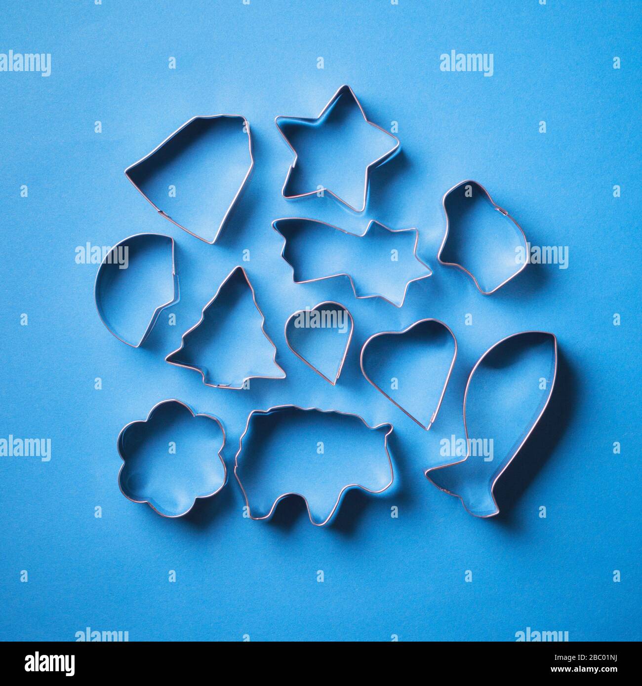 Metal molds for cookies on a blue background. Festive shaped pastry molds for making decorated dessert. With bright contrasting backlight. Stock Photo
