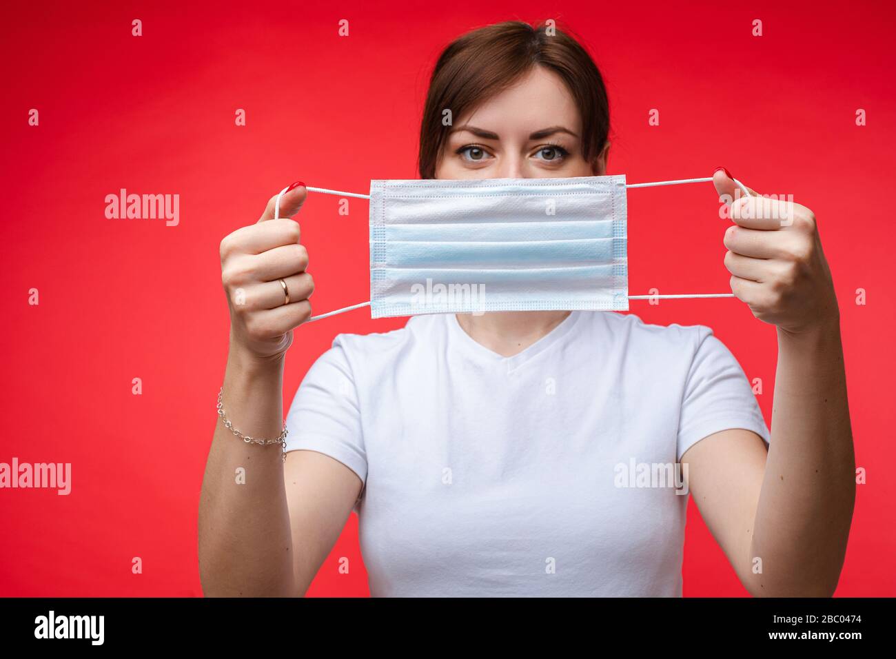 Woman with aseptic mask in hands. Isolate on red. Stock Photo