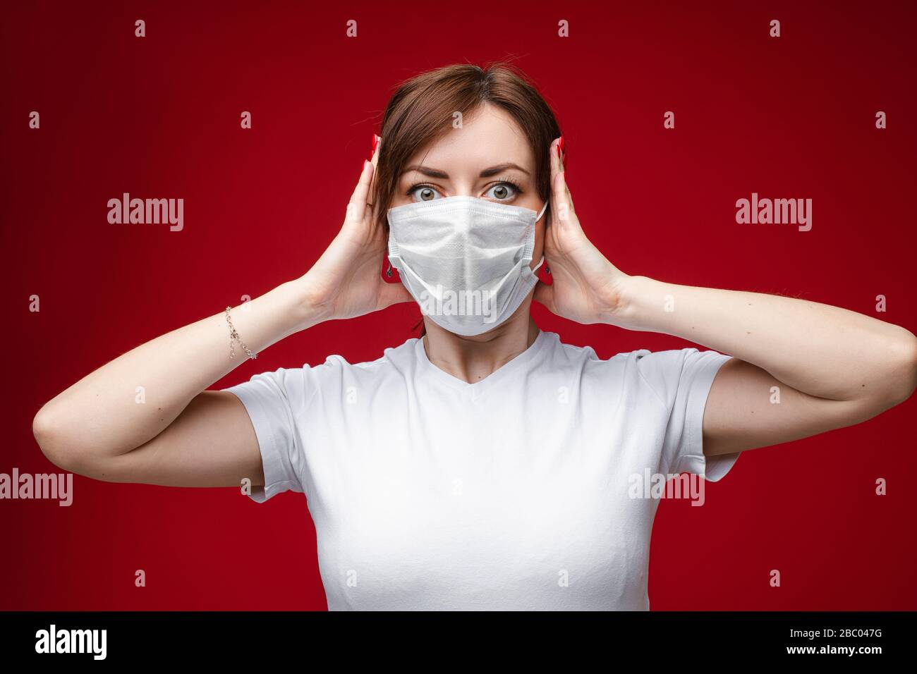 Woman in mask is shocked with hands at ears. Stock Photo