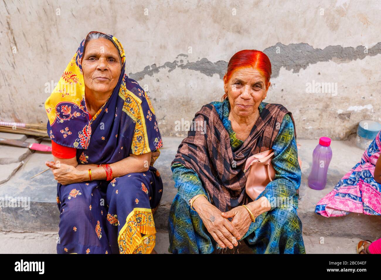 Street scene in Mahipalpur district, a suburb near Delhi Airport in New Delhi, capital city of India: old women sitting at the side of a street Stock Photo